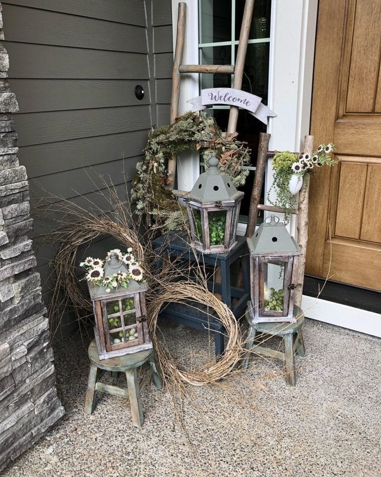 porch vignette using old rustic items including lanterns, wooden stools, wooden ladder, and a wreath next to a front door