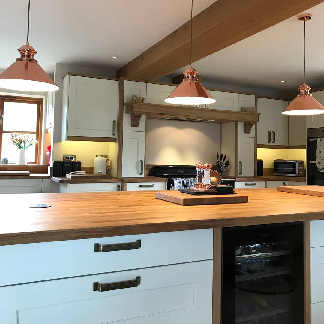 Modern kitchen with wooden countertops, white cabinets, and copper pendant lights, embodying practical ways to add natural elements to your home. Features include a wine fridge, oven, and kitchen utensils.