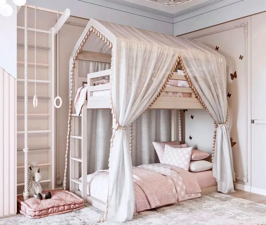 A child's bedroom fit for a princess with a bunk bed styled as a tent, featuring a ladder, slide, and curtains. The lower bunk has pink bedding and pillows. A plush unicorn toy sits on a cushioned mat nearby, making it one of the 17 Pink Bedrooms Fit for a Princess.