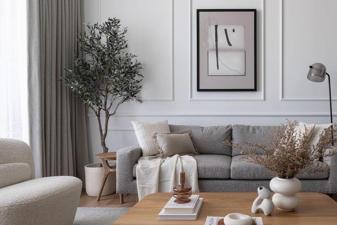 A modern living room featuring a gray sofa, decorative plants, framed abstract artwork on the wall, and a small coffee table with books and vases. Discover our Top 10 Tips for Creating a Minimalist Living Room.