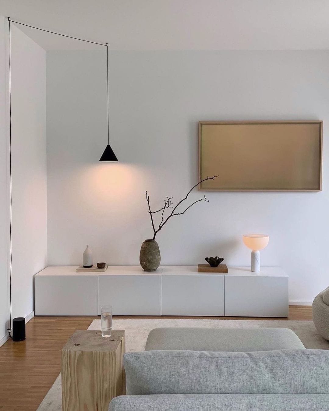 Minimalist living room with a white bench, hanging pendant light, Top 10 Tips for Creating a Minimalist Living Room items, and a wooden stool.