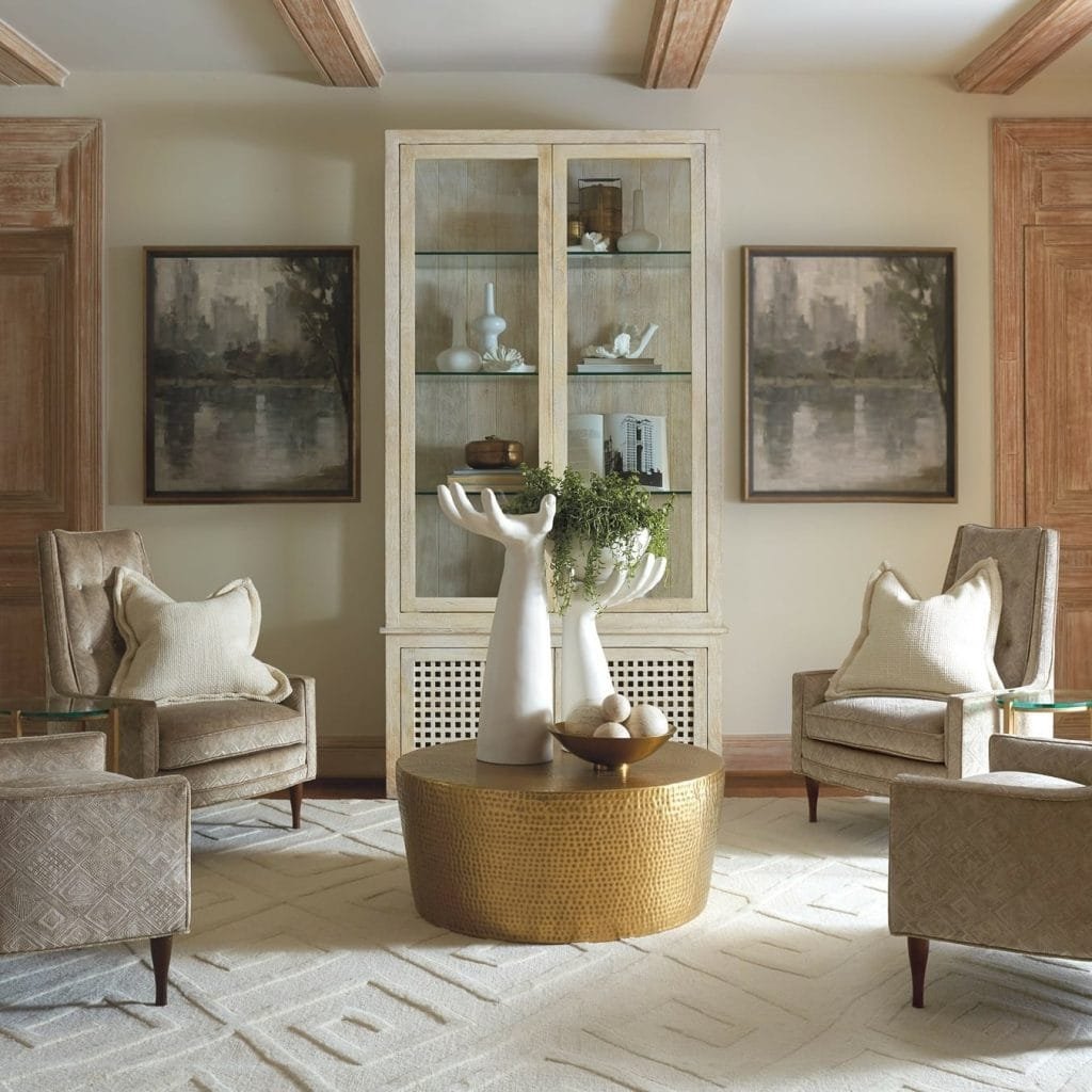 Elegant living room with two upholstered chairs, a round gold coffee table, a funky cabinet, and abstract paintings on the walls.