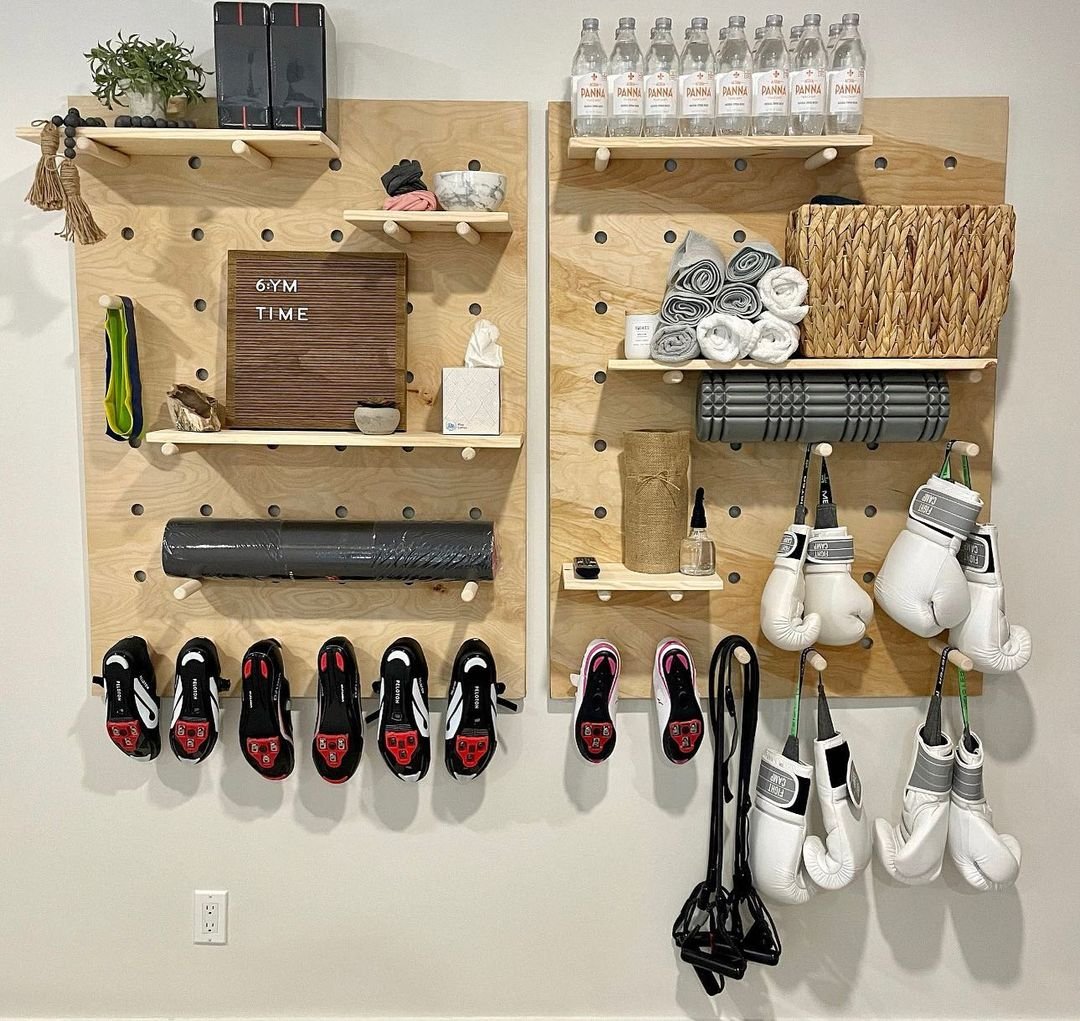 A neatly organized gym wall featuring shelves with water bottles, towels, gloves, shoes, and various workout equipment demonstrates how to make organization stylish with a wall pegboard.