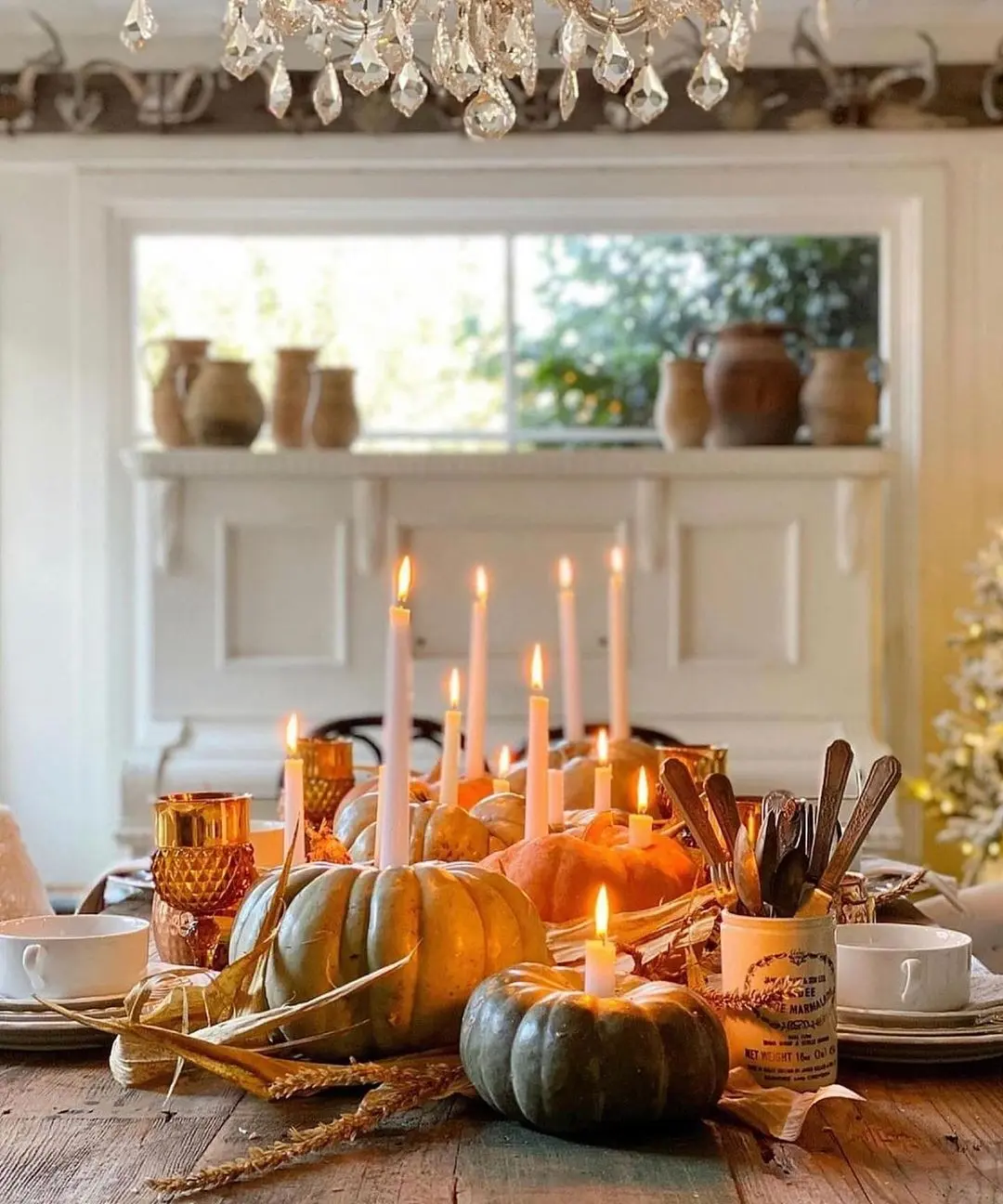 A dining table adorned with lit candles, pumpkins, and autumnal items captures the essence of embracing hygge. Set in a room featuring a window and vases on the mantelpiece, it showcases cozy fall decor ideas for a blissful home.