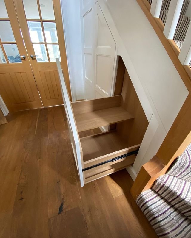 A wooden staircase with a pull-out drawer seamlessly integrated underneath, revealing two compartments for storage—truly an under stairs pantry: a dream storage solution for small kitchens.