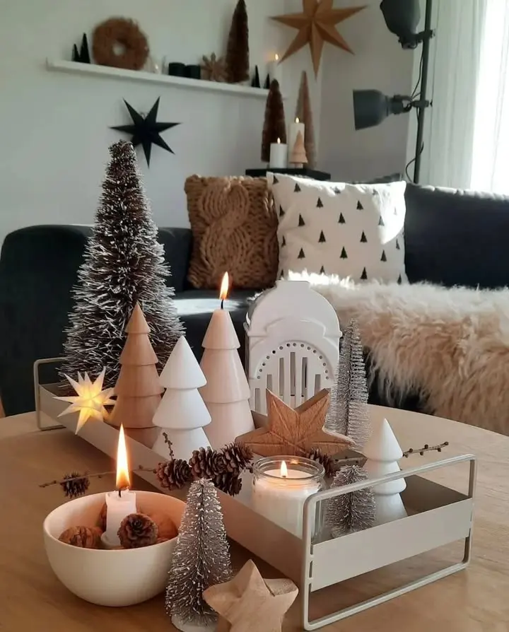 A living room decorated with minimalist Christmas ornaments, pine trees, and candles embraces the season: how to transition your home decor from fall to winter with neutral-toned pillows and a cozy faux fur throw on the sofa.