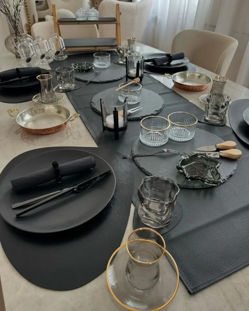 A dining table set with black placemats, plates, glasses, and napkins features gold-rimmed glassware and minimalist magic—perfect inspiration for styling a simplified winter table decor arranged neatly for a cozy meal.