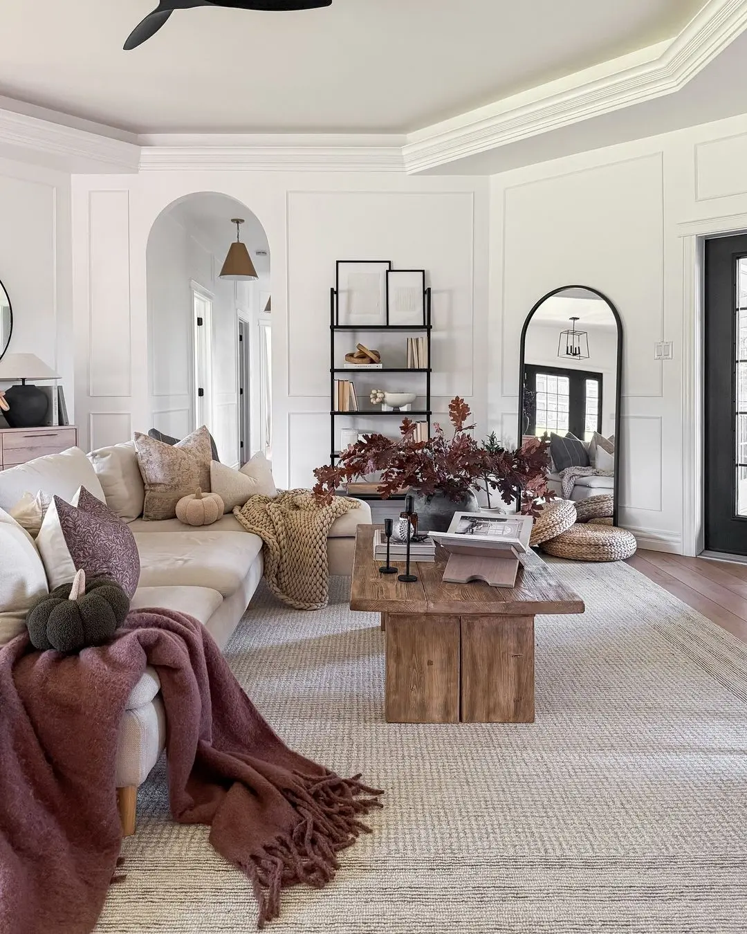 A modern living room with a beige sectional sofa, wooden coffee table, and neutral-toned decor illustrates how to avoid common mistakes when decorating for seasonal changes—blend cozy throw blankets, pillows, and wall shelves for year-round style.