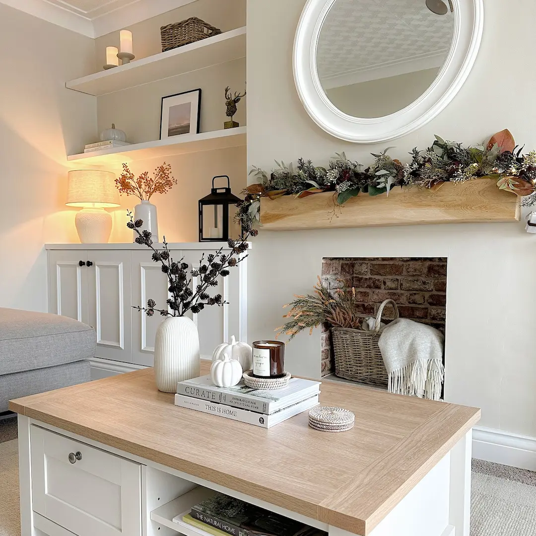 A bright, neutral-toned living room with a wooden coffee table, decorative vases, and a mirror above a brick fireplace—showcasing how to avoid common mistakes when decorating for seasonal changes.