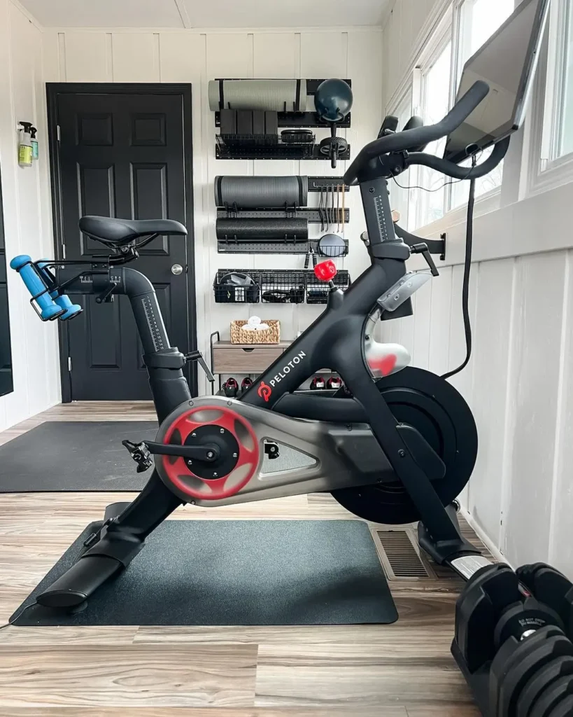 Transform your space with a Peloton exercise bike in a well-designed home gym, complete with organized weights and exercise mats on the wall. For more ideas, check out "How to Design the Perfect Home Gym: Tips for Every Space.