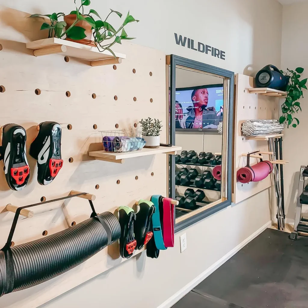 Home gym with pegboard storage, perfectly designed for any space. Featuring cycling shoes, bands, mats, and plants. Mirror labeled "WILDFIRE" reflects exercise equipment—tips for creating your ideal workout environment.