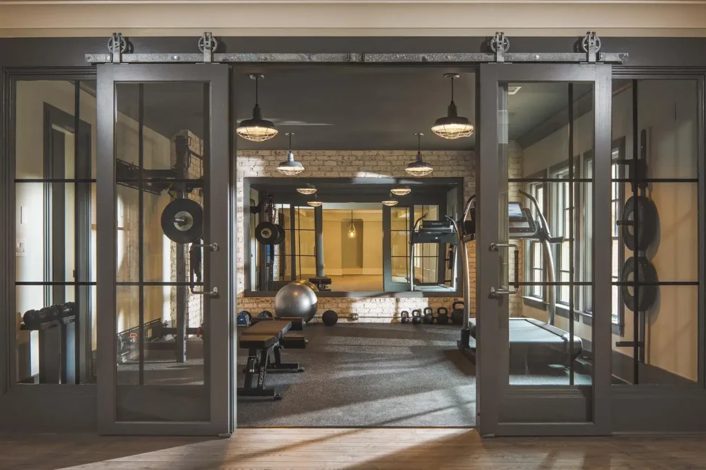 A modern home gym with glass double doors, weight racks, benches, kettlebells, and fitness equipment arranged neatly on a carpeted floor—an inspiring example of How to Design the Perfect Home Gym: Tips for Every Space.