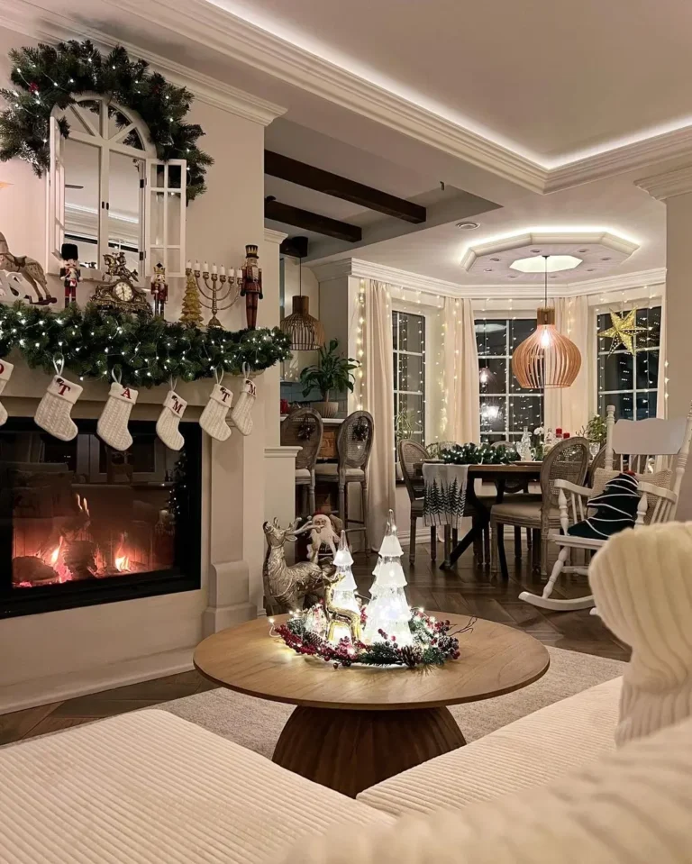 A cozy living room decorated for Christmas with stockings on the fireplace, a lit fire, festive ornaments, and a dining table set near large windows—one of 10 Cozy Christmas Living Room Ideas You’ll Love This Year.