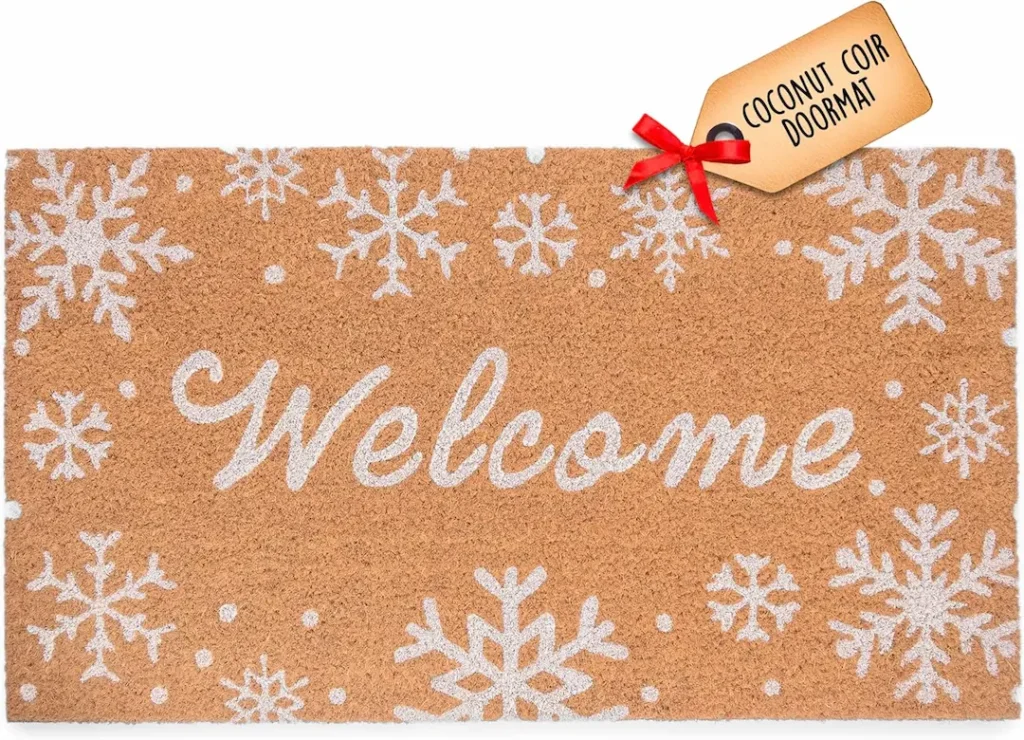 A rectangular doormat with "Welcome" in white script and snowflake designs, made from coconut coir material with a labeled tag—one of the Best Winter Doormats to Refresh Your Porch Décor.