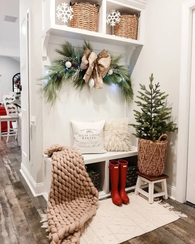 A holiday-themed entryway featuring Holiday Mudroom Decor: Simple Ideas to Impress Your Guests, like a small Christmas tree in a woven basket, red rain boots, a chunky knit blanket, cozy cushion, and festive shelves with baskets and greenery.
