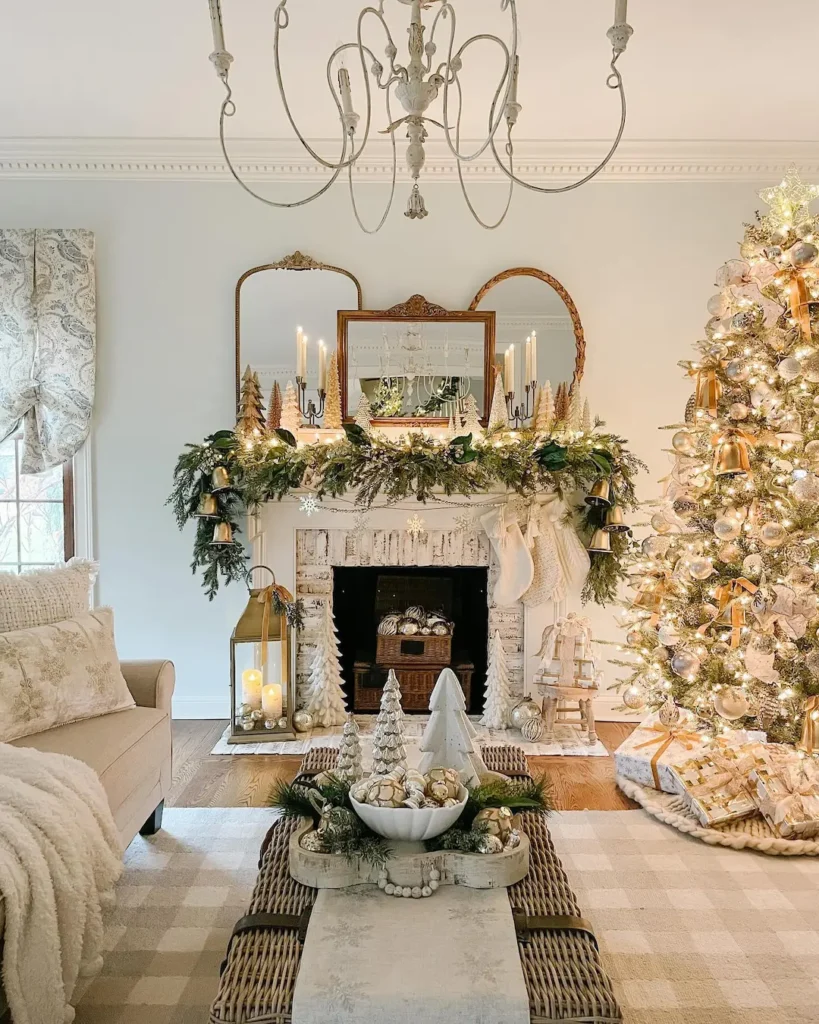 A living room decorated for Christmas with a lit tree, garland and candles on the mantle, and ornaments on the coffee table in neutral and gold tones—one of 10 Cozy Christmas Living Room Ideas You’ll Love This Year.