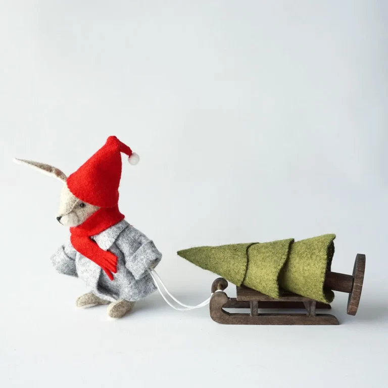 A felt rabbit wearing a red hat and gray coat pulls a small sled carrying a green felt Christmas tree—one of 10 adorable kid-friendly Christmas decorations you’ll love.