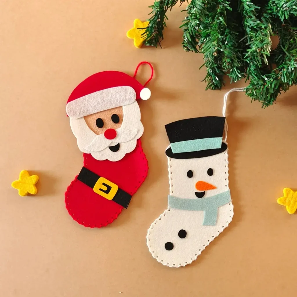 Two felt Christmas stockings, one as Santa Claus and the other as a snowman, rest on a brown surface with yellow star decorations and green pine branches—perfect for any list of 10 Adorable Kid-Friendly Christmas Decorations You’ll Love.