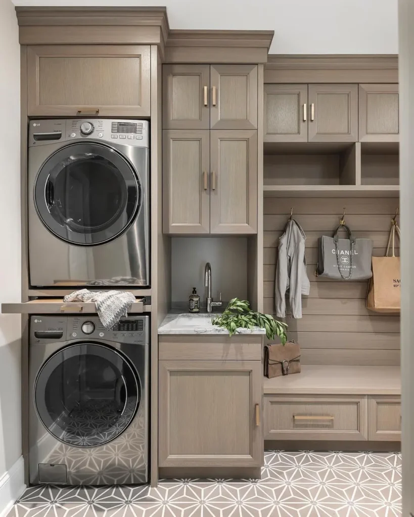 a stackable washer and dryer integrated into beautifully made cabinets in a mudroom with a small sink and alcove bench