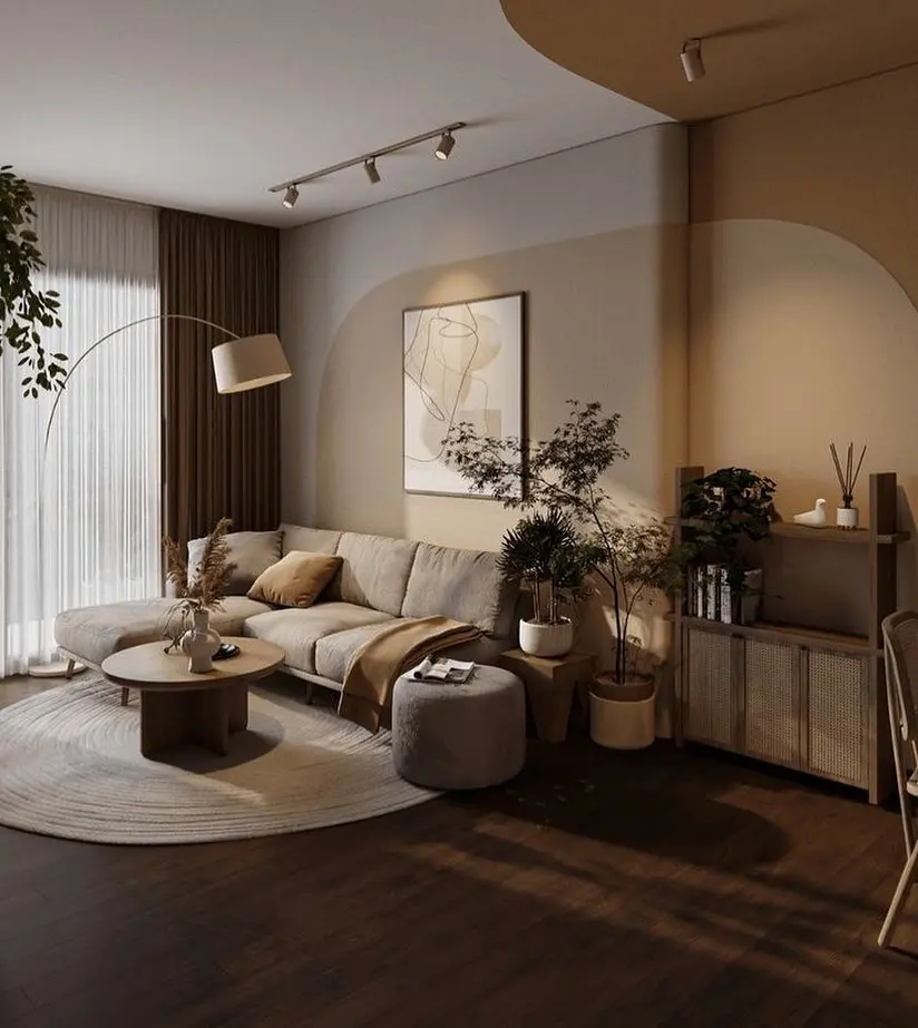 A modern living room with a beige sectional sofa, round coffee table, indoor plants, abstract wall art, and soft lighting, featuring fall-inspired neutral tones and organic modern decor.