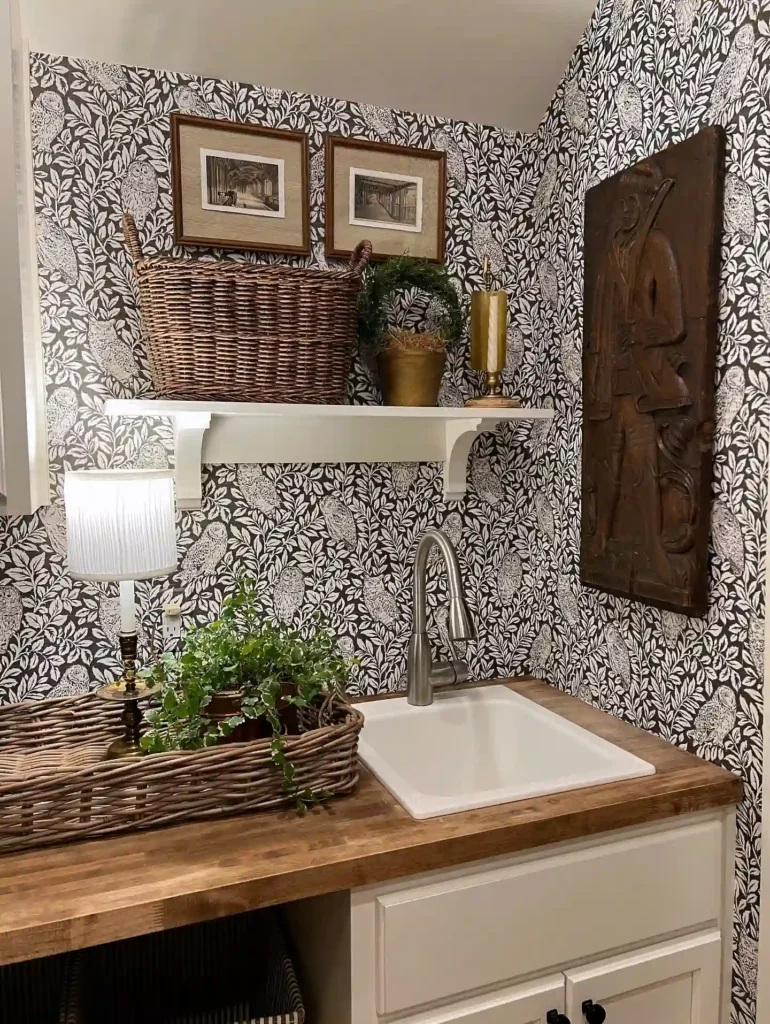 Laundry room decor with bold floral wallpaper, wood countertop, white sink, woven baskets, and vintage wall art.